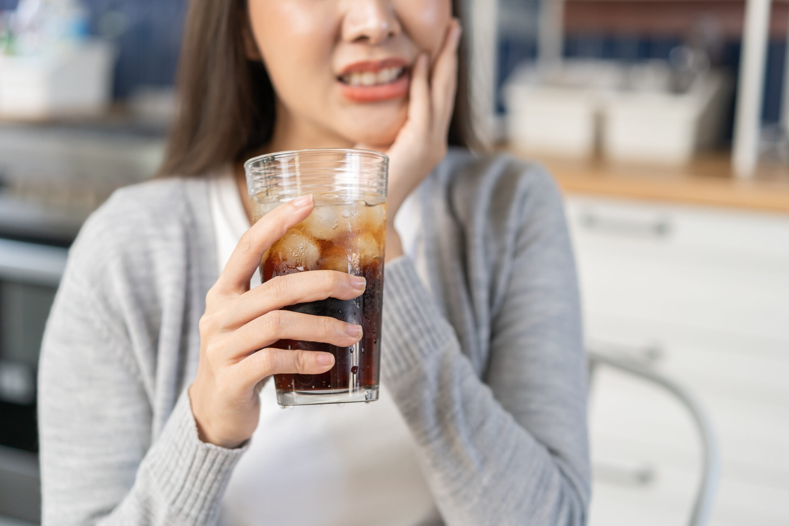 Smiling woman holding an iced drink on a sunny day, symbolizing relief from sensitive teeth in summer